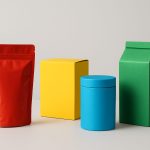 Colorful packaging containers including a red pouch, yellow box, blue cylinder, and green carton on a neutral background