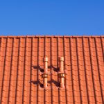 Close-up view of a red-tiled roof with two ventilation pipes against a clear blue sky
